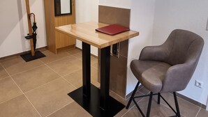 Una habitación con una mesa de madera, una silla, un perchero y un espejo.