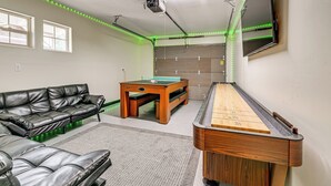 Ein Raum mit Pooltisch, Billardtisch, einer Ledercouch und einem an der Decke befestigten Projektor.