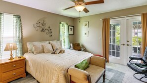 A bedroom with a bed, a nightstand, a chair, a desk, a ceiling fan, and a door leading to a balcony. - Private Yard, Lanai! Pet-Friendly Fort Pierce Home (Fort Pierce)