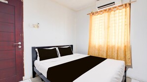 A room with a bed, a door, an air conditioning unit, and a window with curtains.
