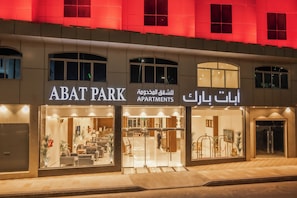 Un edificio con el rótulo 'ABAT PARK APARTMENTS', amplias ventanas de vidrio y una entrada bien iluminada.
