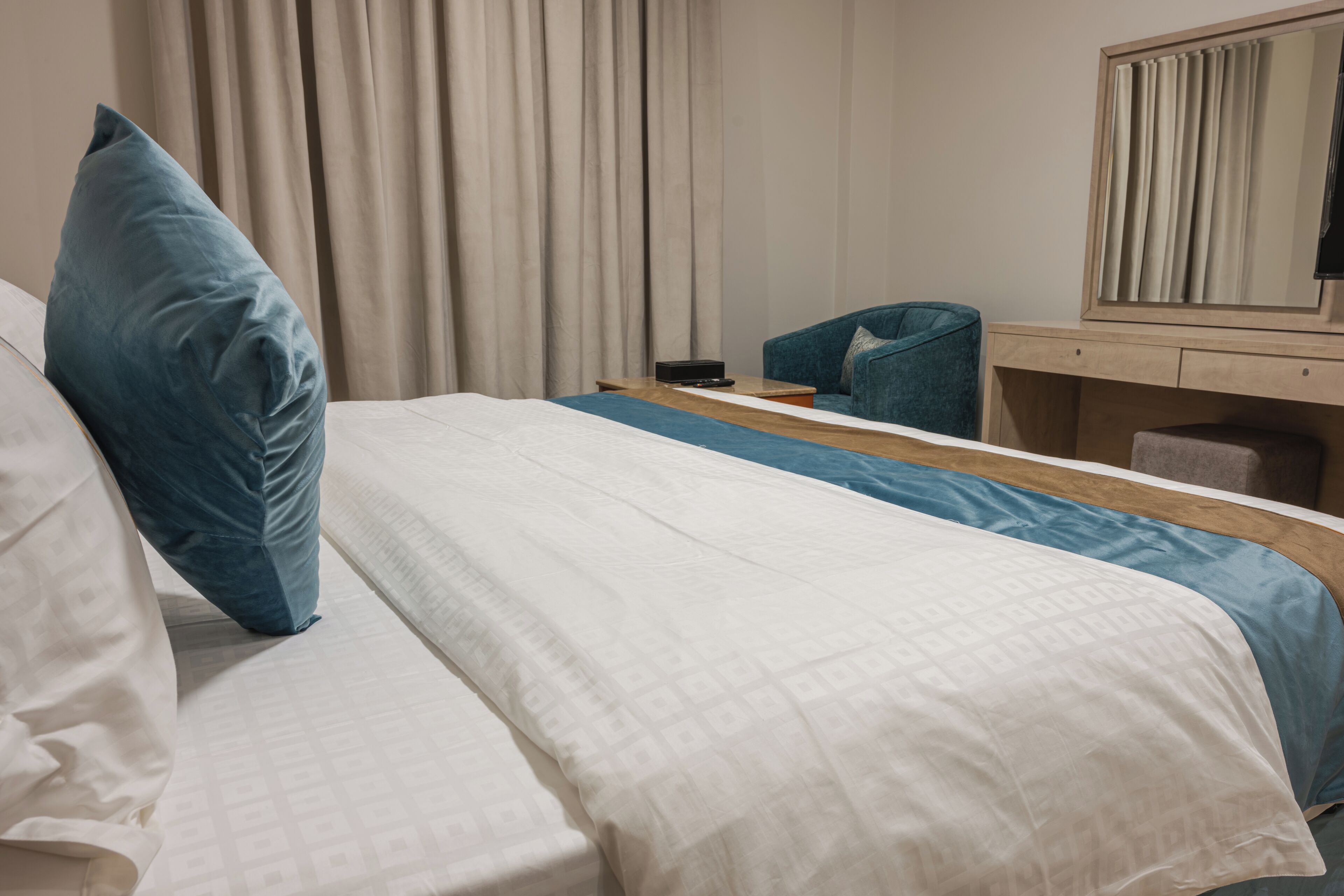 A hotel room with a bed, a desk, a chair, a mirror, and curtains.