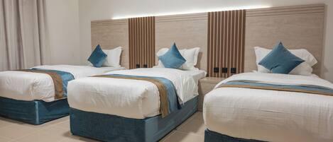 Habitación de hotel con tres camas, cada una con cabecera azul, ropa de cama blanca y detalles en marrón.