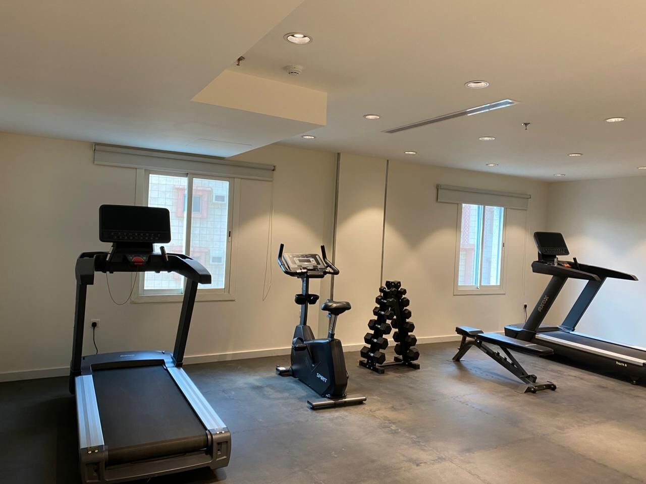 A home gym with treadmills, an elliptical, and a set of dumbbells.