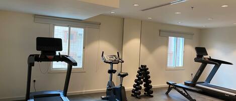 Een sportschool thuis met loopbanden, een elliptische trainer en een set gewichten.