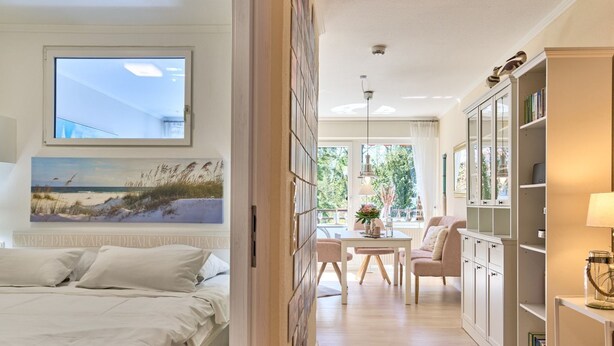 A bedroom with a bed, a painting of a beach, and a view of the outdoors through a window. - LichtSpiel Scharbeutz - Arrive, take a deep breath, enjoy - Apartment LichtSpiel (Scharbeutz)