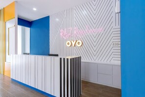 Uma receção com um letreiro de néon que diz 'RAZ Residence OYO' num interior moderno com padrões geométricos nas paredes e uma parede de destaque azul.