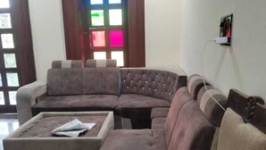 Un salon avec un canapé d’angle, une petite table sur laquelle se trouvent des papiers et une prise électrique fixée au mur.