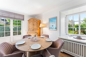Ein Esszimmer mit einem runden Tisch, gedeckt für sechs Personen, einem Holzschrank, einer Lampe und einem gerahmten Bild.