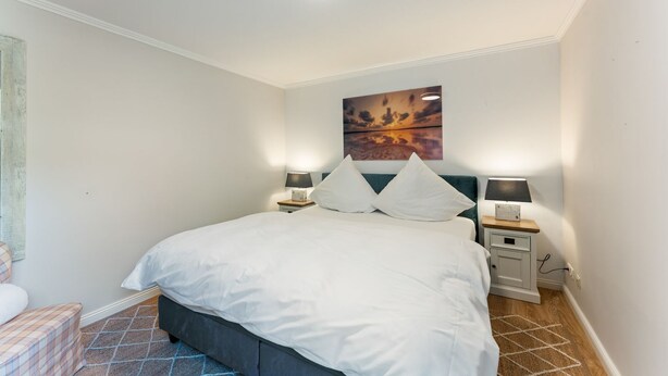 A bedroom with a bed, two bedside tables with lamps, a wall-mounted artwork, and a patterned rug. - Stadum Hüs - Charming vacation home for four people with its own garden in (Westerland)