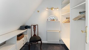 A walk-in closet with a radiator, a chair, and a shelf unit. - Stadum Hüs - Charming vacation home for four people with its own garden in (Westerland)