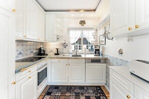 A kitchen with white cabinets, a patterned rug, and a coffee machine. - Stadum Hüs - Charming vacation home for four people with its own garden in (Westerland)
