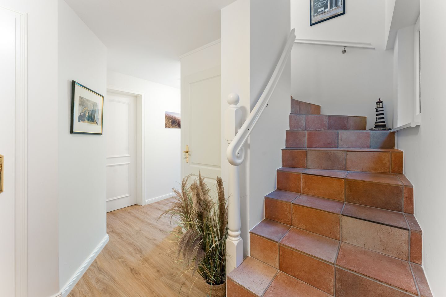 Una escalera con baldosas de terracota, una pared blanca y un cuadro enmarcado encima.