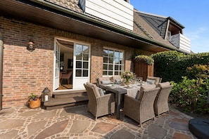 A brick house with a patio, outdoor seating, and a large window. - Stadum Hüs - Charming vacation home for four people with its own garden in (Westerland)