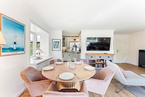 A modern dining area with a round table, chairs, and a television in the background. - Stadum Hüs - Charming vacation home for four people with its own garden in (Westerland)