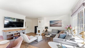 A modern living room with a flat-screen TV, a fireplace, a sofa, a coffee table, and a dining area with a table and chairs. - Stadum Hüs - Charming vacation home for four people with its own garden in (Westerland)
