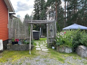 Une porte en bois portant l’inscription « Appartement familial » donne sur un sentier bordé de verdure et menant à un petit abri de jardin.