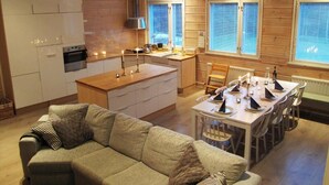 Una habitación acogedora de estilo cabaña, con kitchenette, una mesa de comedor preparada para cuatro personas y un sofá con cojines.