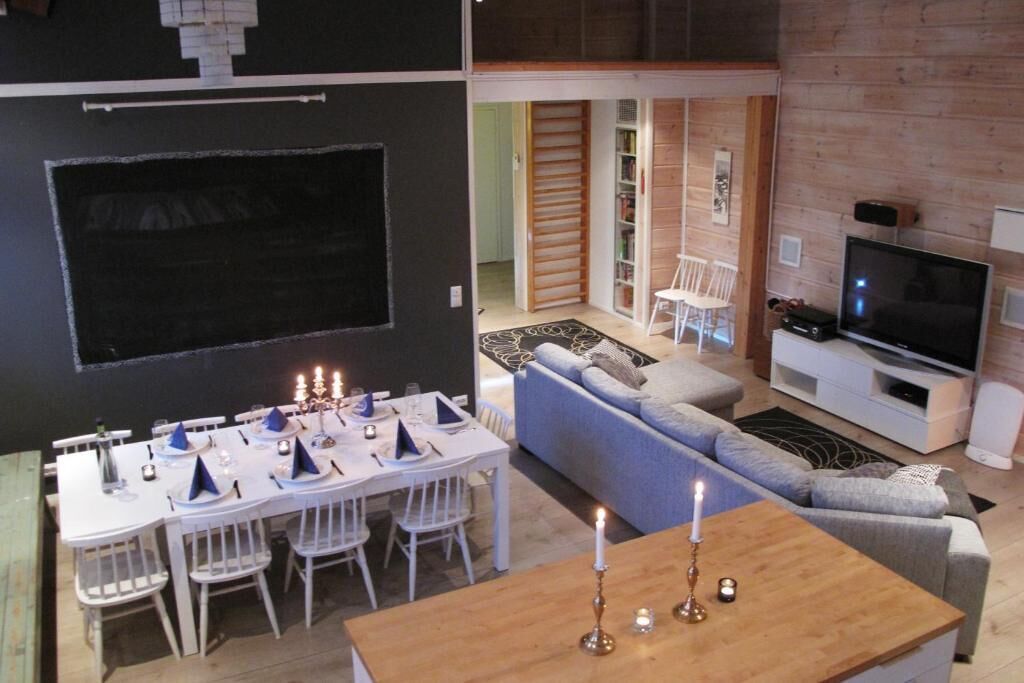 Uma sala de jantar com mesa posta para seis lugares, sofá, TV e estante em um interior moderno.