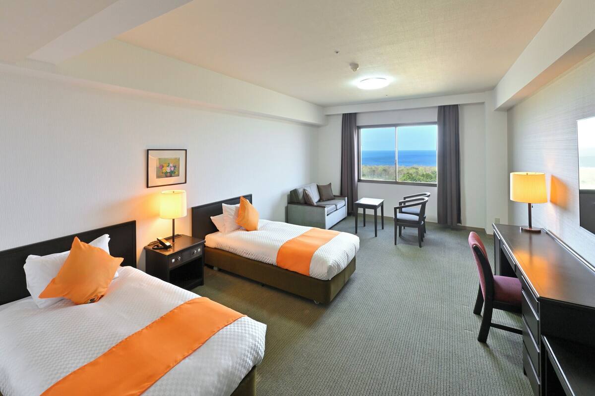Une chambre d’hôtel avec deux lits, un bureau, une chaise, une télévision et une grande fenêtre donnant sur un beau paysage.