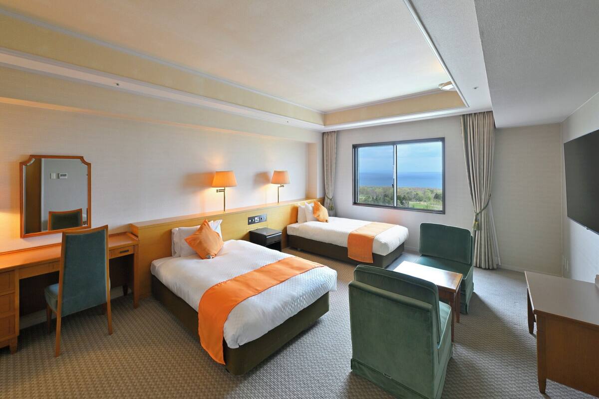 Une chambre d’hôtel avec deux lits, un bureau, une chaise, une télévision et une fenêtre donnant sur un beau paysage.