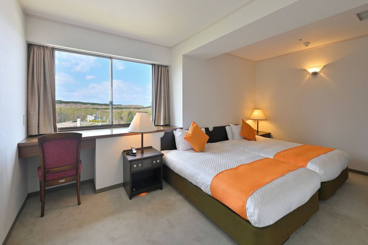 Une chambre d’hôtel équipée d’un lit, d’un bureau, d’une chaise et d’une fenêtre donnant sur un paysage agréable.