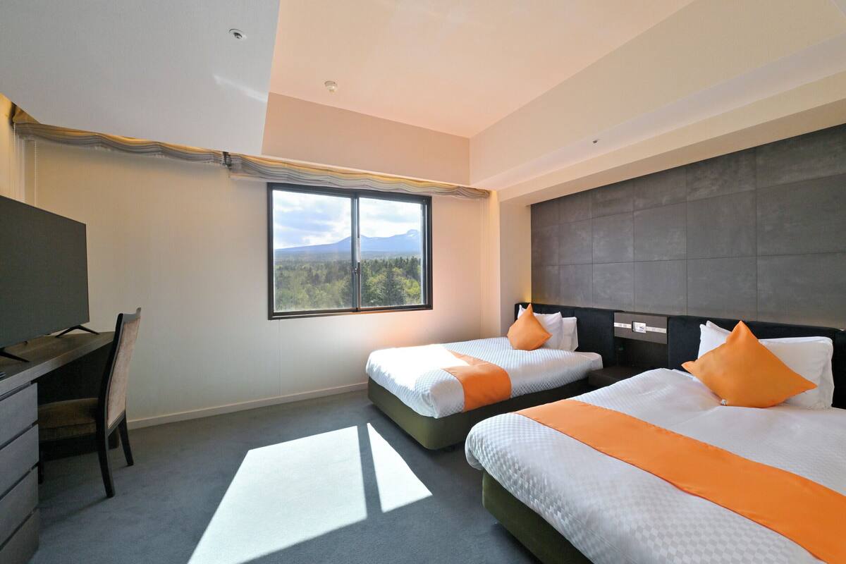 Une chambre d’hôtel avec deux lits, un bureau et une grande fenêtre donnant sur la montagne.
