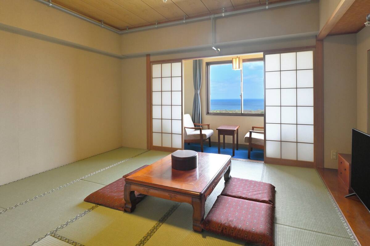 Une pièce de style japonais traditionnel, avec un sol recouvert de tatamis, une table basse, deux coussins et un téléviseur.