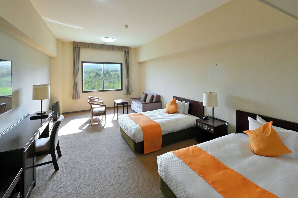 Une chambre d’hôtel avec deux lits, un bureau, une chaise, une petite table et une fenêtre donnant sur un beau paysage.