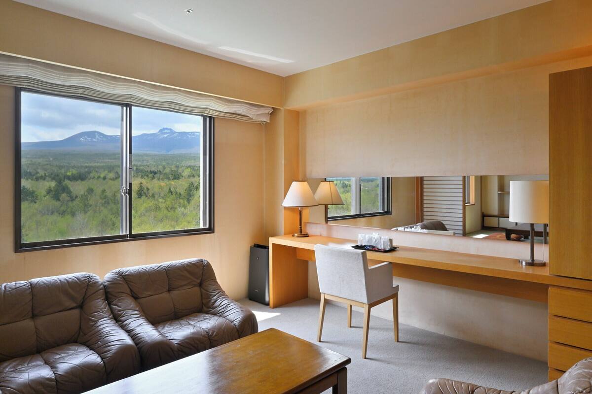 Une chambre d’hôtel avec une grande fenêtre, un bureau, une chaise, un canapé et une table.