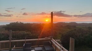 A wooden deck with steps leading to a viewing area overlooking a coastal landscape during sunset.