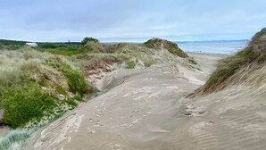 A sandy beach path with footprints, surrounded by grassy dunes and a distant view of the sea.
