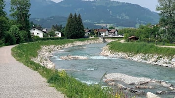 A gravel road alongside a river with houses and mountains in the background.