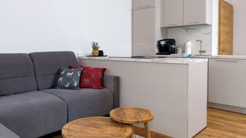 Un espace de vie moderne avec un canapé gris, des tables d’appoint en bois, un îlot de cuisine et une porte en bois.