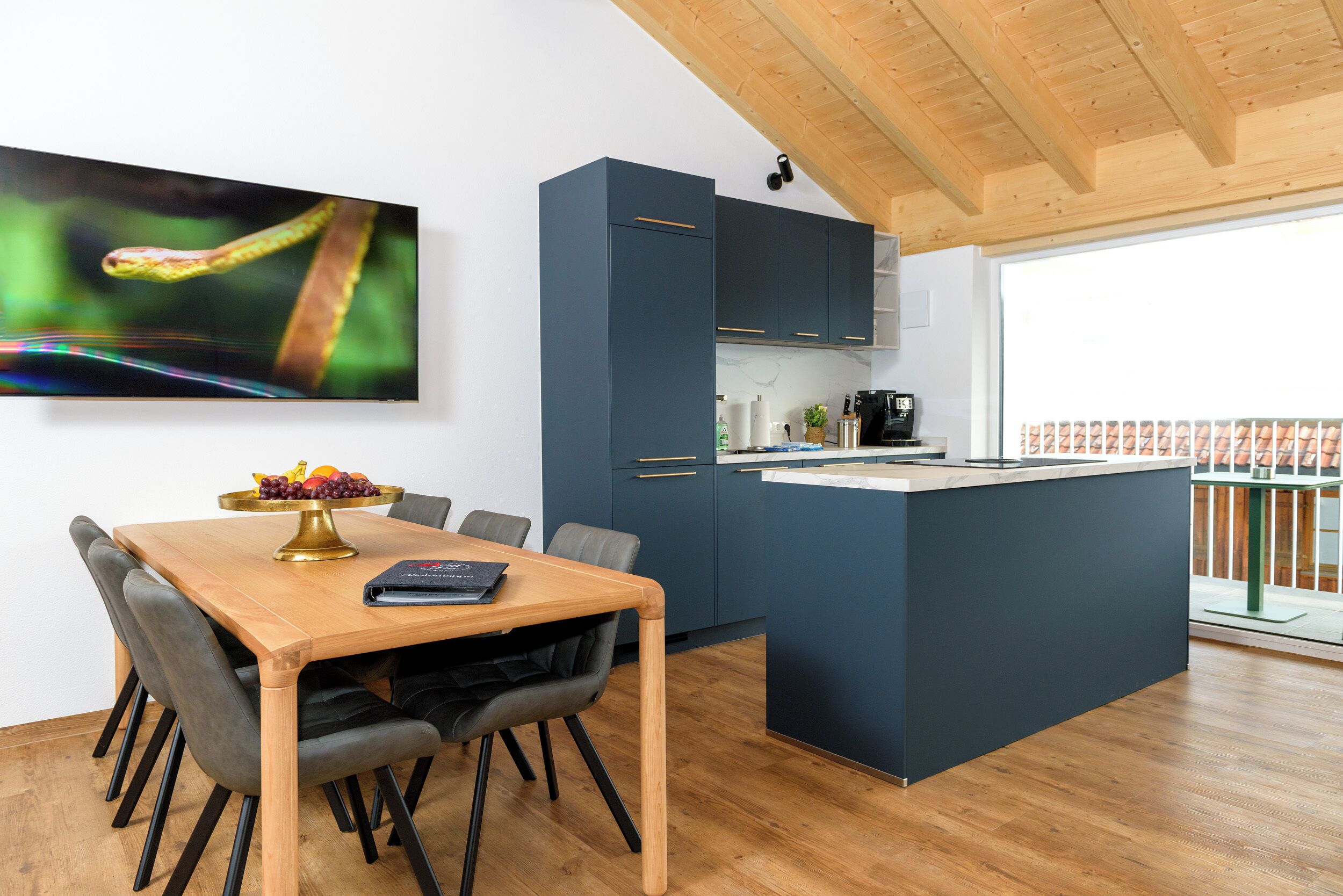 Een moderne keuken met donkere kastjes, een houten eettafel en een groot kookeiland.