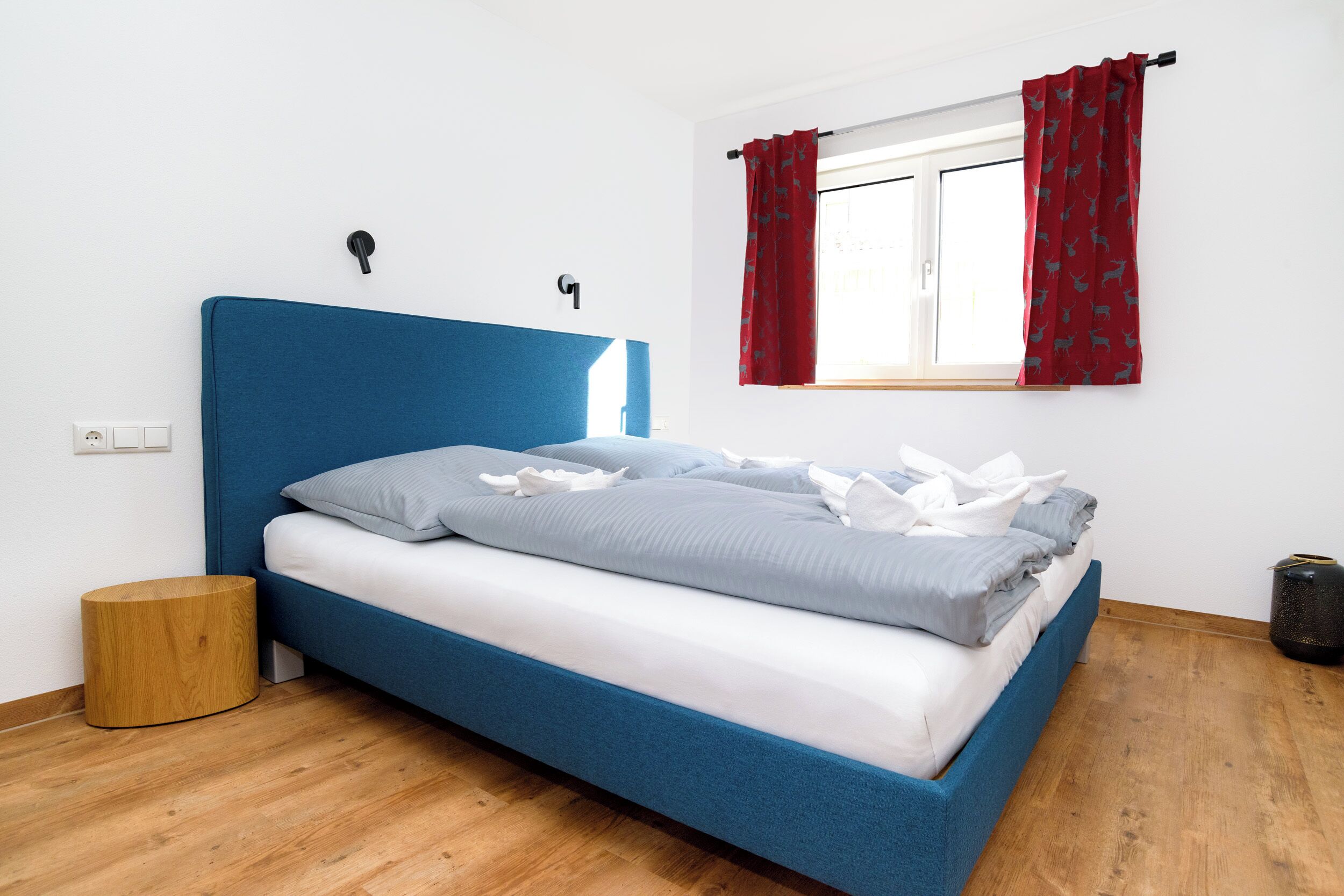 Una cama con cabecera azul, ropa de cama blanca y cortinas rojas.
