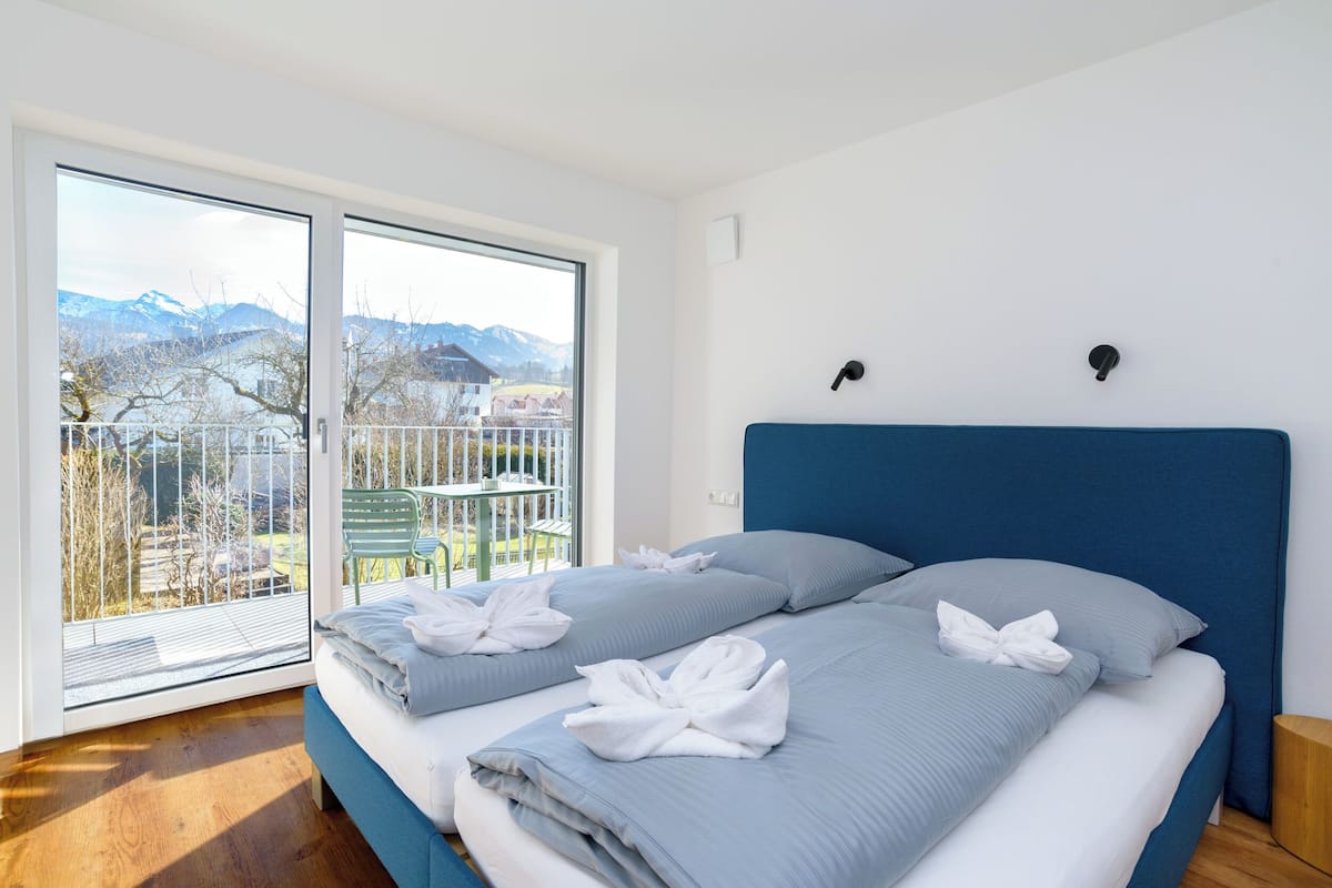 Une chambre avec une grande fenêtre, un lit avec une literie bleue et une vue sur les montagnes.