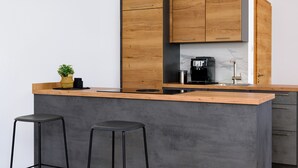 Una cocina moderna con armarios de madera, encimera de mármol, una cafetera y dos taburetes de bar.