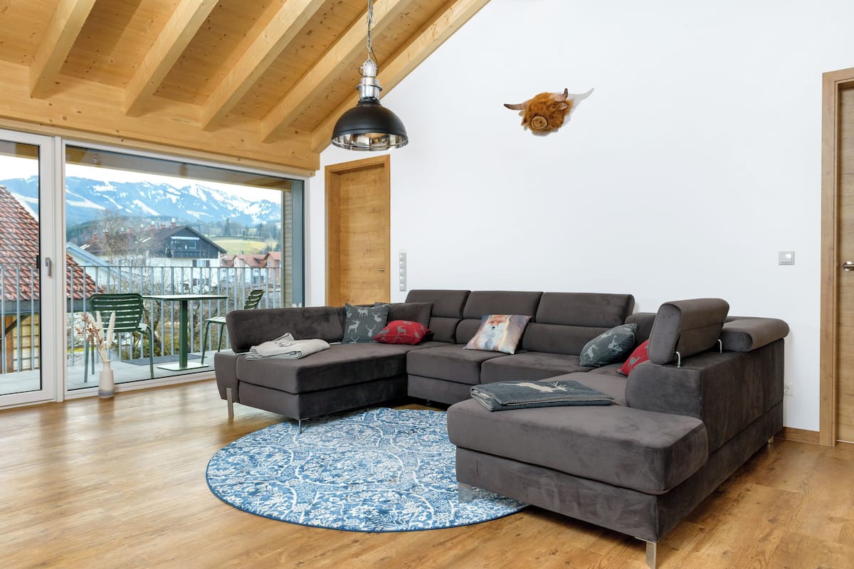 Un salon moderne avec un canapé d’angle, un tapis rond bleu et un plafond en bois.