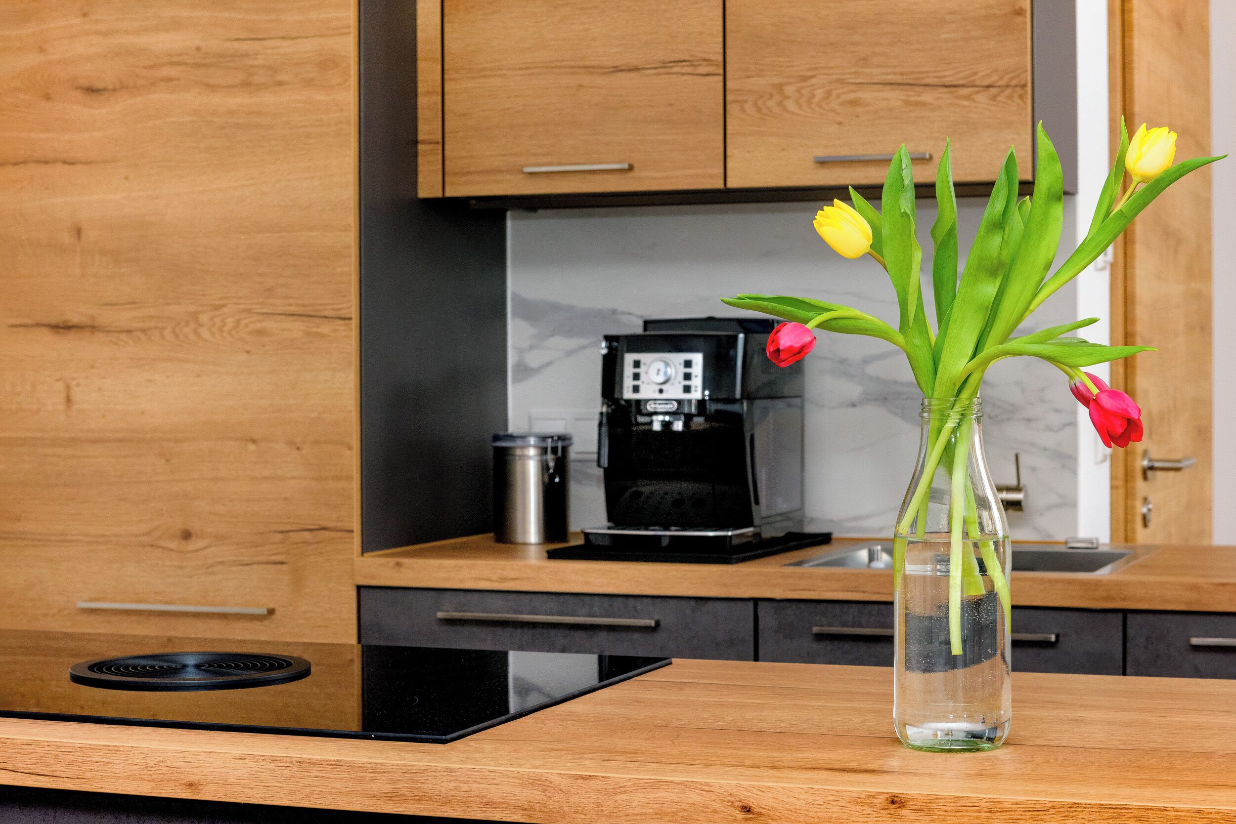 A modern kitchen with wooden cabinets, a coffee maker, and a vase with flowers on the counter.