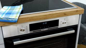 Una cocina con placa de inducción Bosch, un reloj digital y un horno de acero inoxidable.