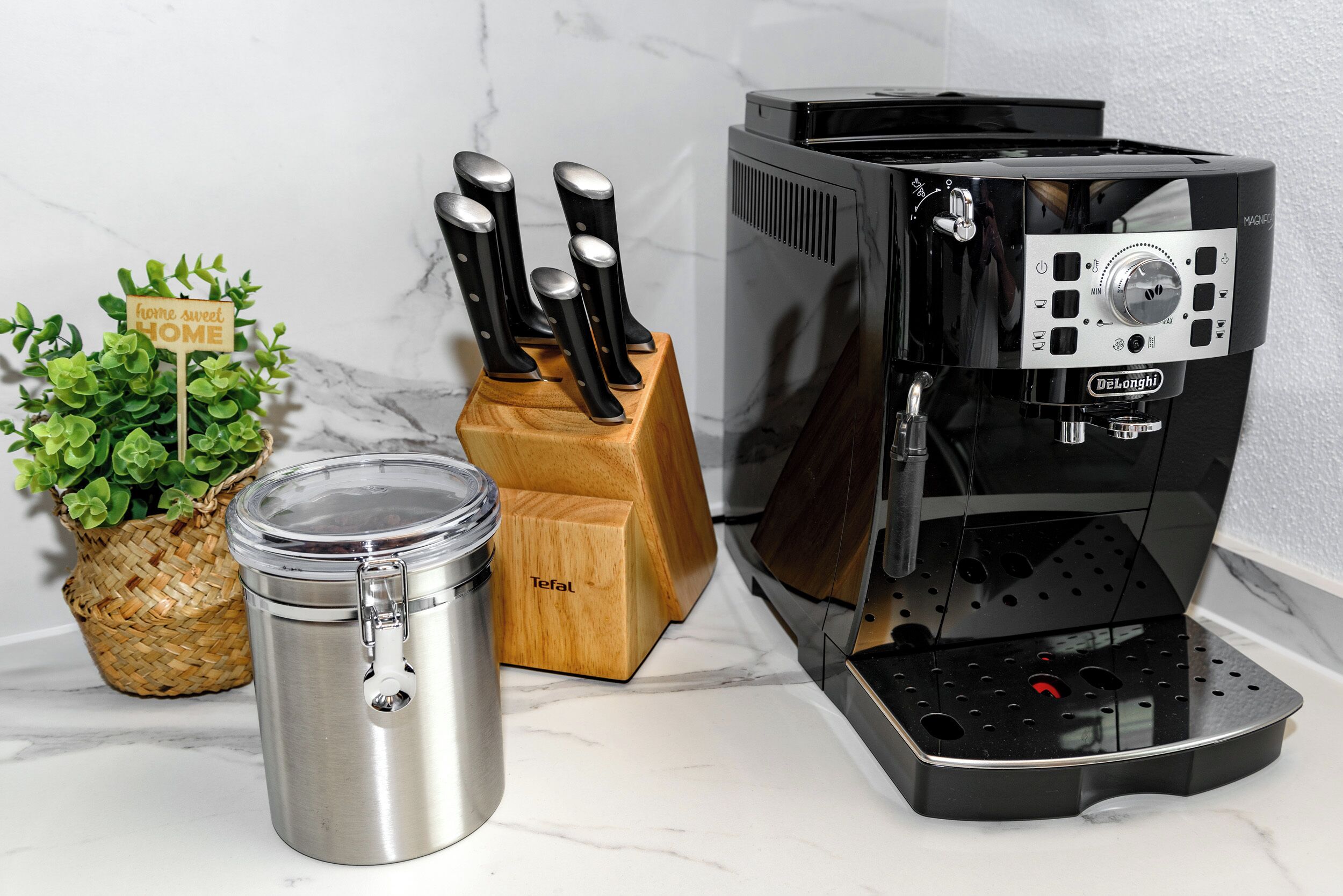 A kitchen with a coffee machine, a knife block, a stainless steel container, and a small potted plant.
