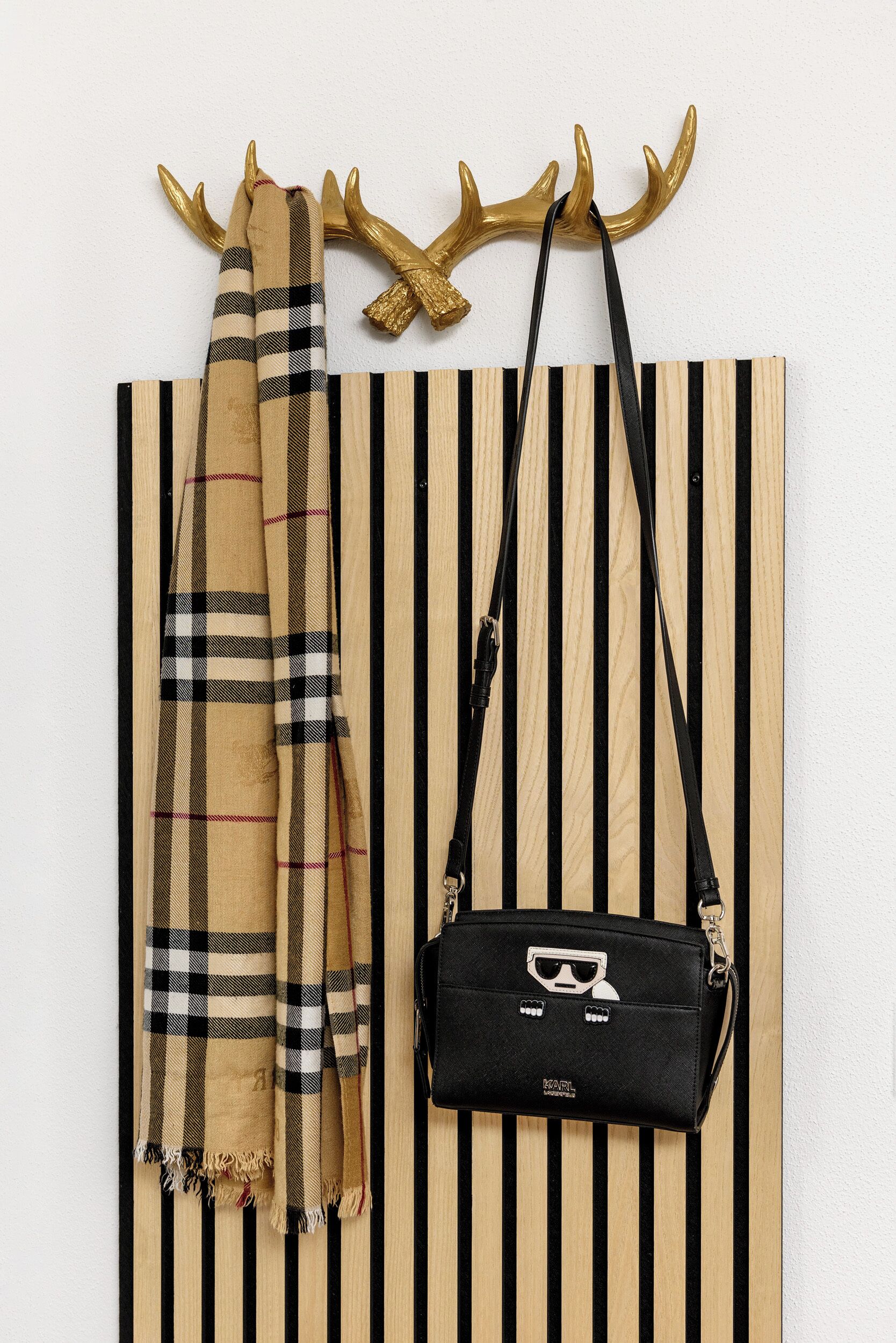 A striped wall with a black and beige scarf and a black bag with sunglasses.