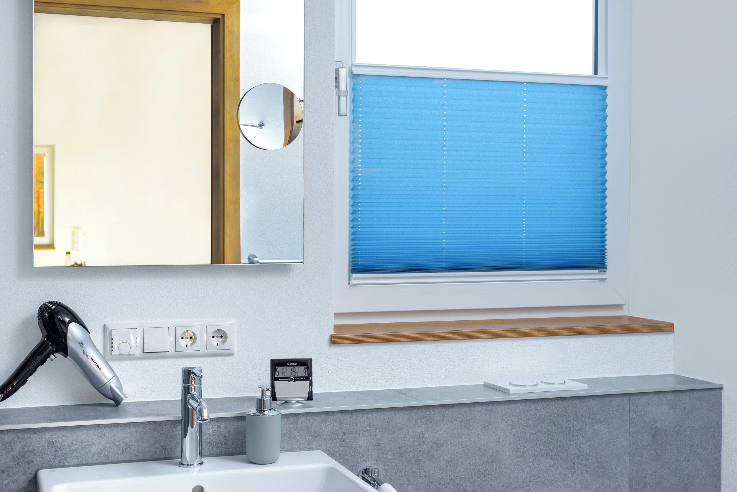 A bathroom with a sink, mirror, hairdryer, and window with blinds.