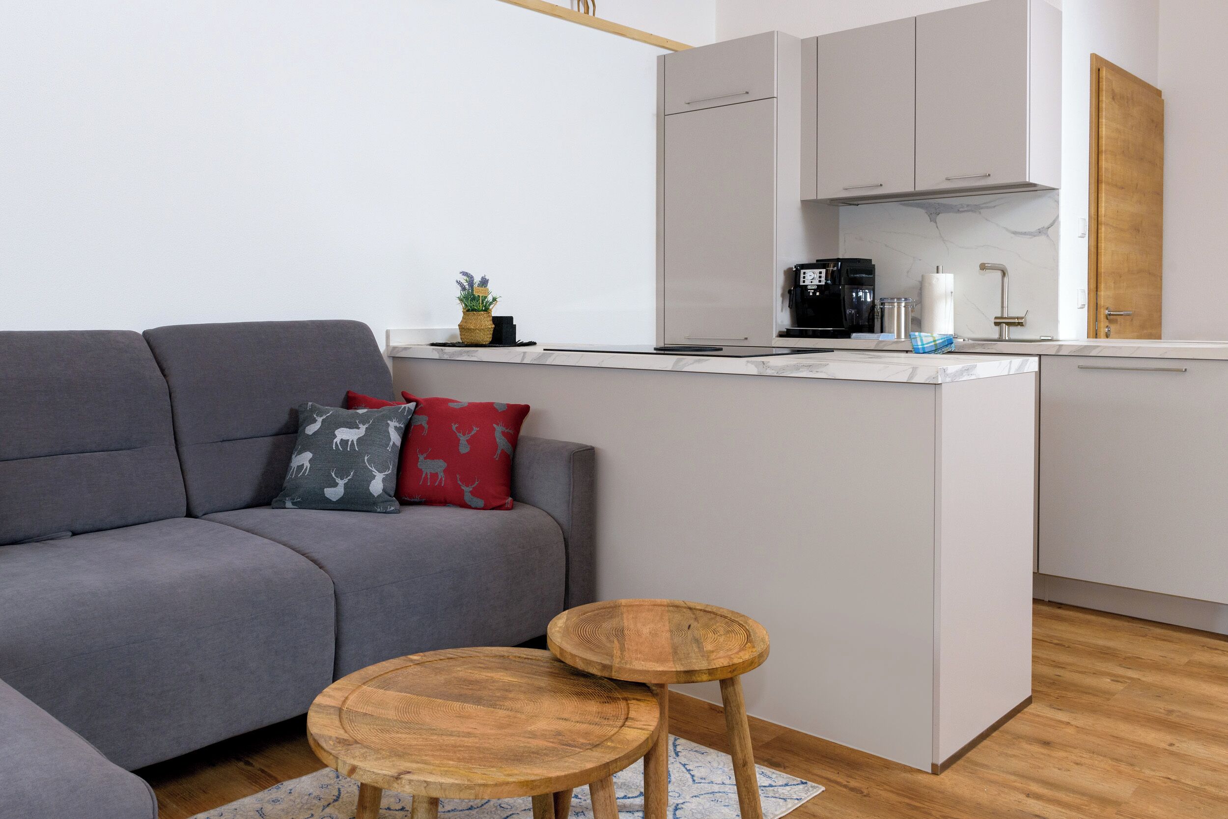 Eine moderne Küche mit weißen Schränken, einem grauen Sofa und einer kleinen Kochinsel mit Barhocker.
