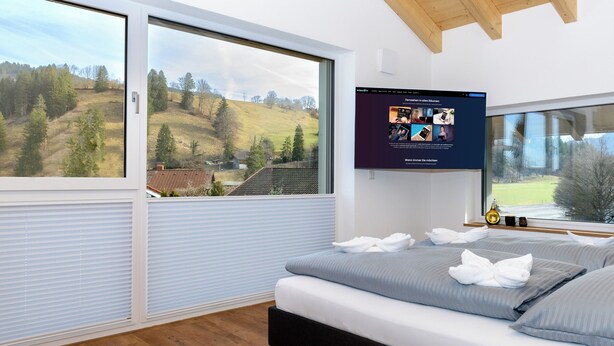 Un dormitorio moderno con una cama grande, un televisor en la pared y vistas panorámicas a través de las ventanas.