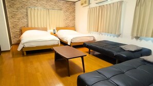 Ein kompaktes Hotelzimmer mit zwei Betten, einer Schlafcouch, einem kleinen Tisch und einer Wanduhr.