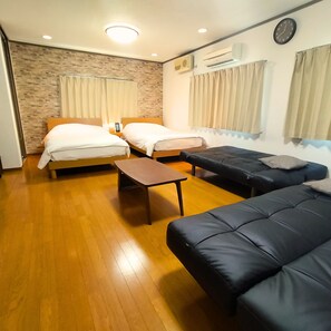 Ein kompaktes Hotelzimmer mit zwei Betten, einer Schlafcouch, einem kleinen Tisch und einer Wanduhr.