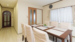Ein Esszimmer mit Holztisch, weißen Stühlen, einer Uhr an der Wand und einer Tür mit satinierten Glasscheiben.