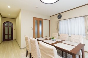 Ein Esszimmer mit Holztisch, weißen Stühlen, einer Uhr an der Wand und einer Tür mit satinierten Glasscheiben.